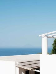 Luxury boutique hotel nestled on a Sicilian cliff, overlooking azure Mediterranean waters with elegant white architecture and lush bougainvillea.