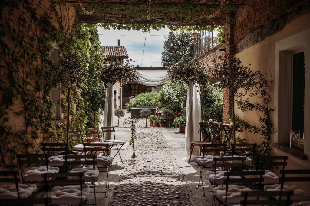 Elegant Italian coastal hotel with white stone facade, blue shutters, surrounded by lush Mediterranean gardens and stunning sea panorama at sunset