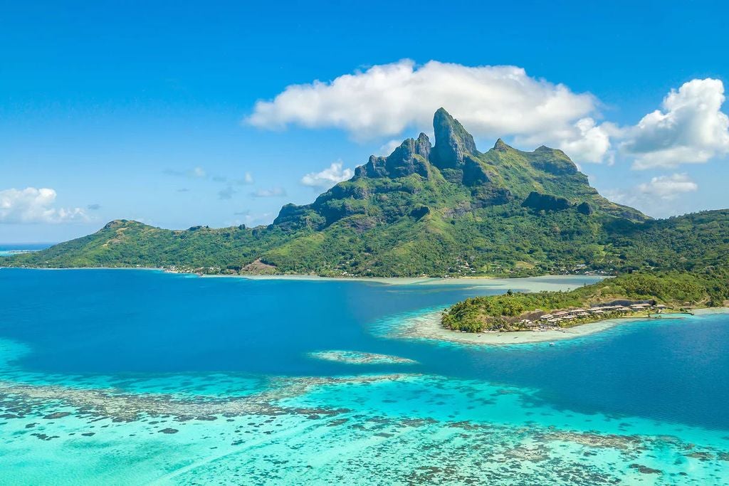 Overwater luxury villas with thatched roofs stretching into crystal-clear turquoise lagoon, backed by Mount Otemanu and palm trees