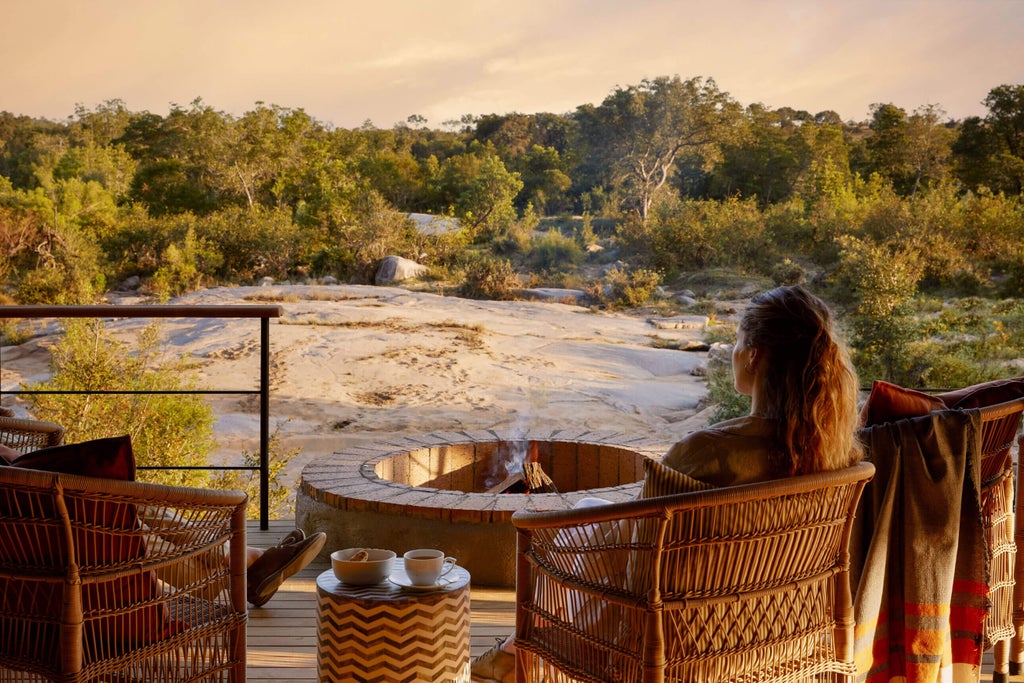 Elegant safari lodge with thatched-roof pavilions overlooking a serene riverbank, surrounded by African bushveld at golden hour