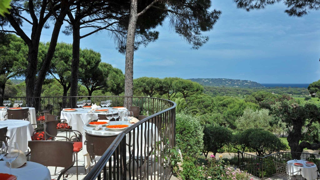 Luxurious white-washed villa with blue shutters nestled in lush Mediterranean gardens, overlooking the scenic coast of Saint-Tropez with elegant poolside setting