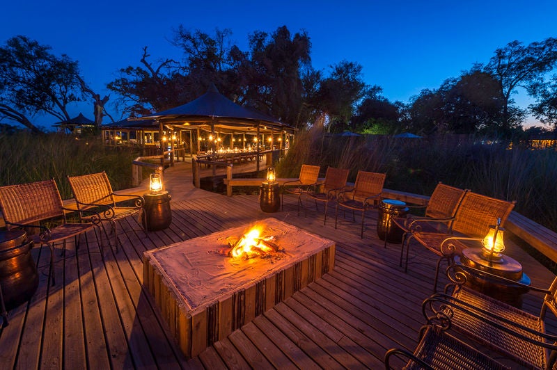 Luxury safari lodge with raised wooden walkways connecting elevated tents overlooking Okavango Delta's waterways and lush savanna