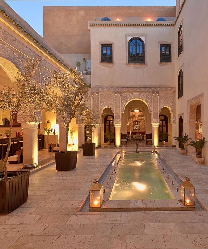 Luxurious Moroccan riad with intricate blue zellige tilework, ornate archways, and traditional courtyard with elegant fountain in Fès