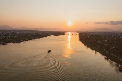 Elegant French colonial-style hotel with white facade, lush tropical gardens, and traditional architecture overlooking a serene river in historic Hue, Vietnam.