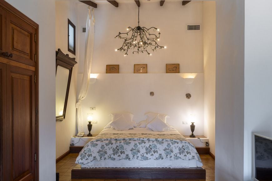 Elegant stone-walled superior hotel room at Ca's Xorc Luxury Retreat, featuring pristine white linens, rustic wooden furnishings, and soft natural lighting from Spanish countryside windows