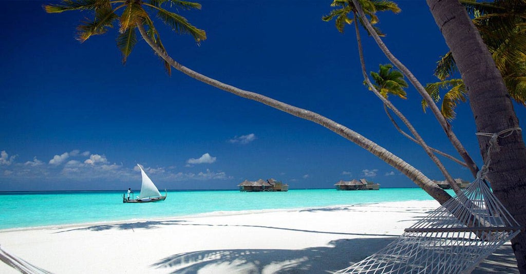 Overwater villa resort with thatched-roof bungalows connected by wooden walkways above crystal-clear turquoise Maldivian lagoon