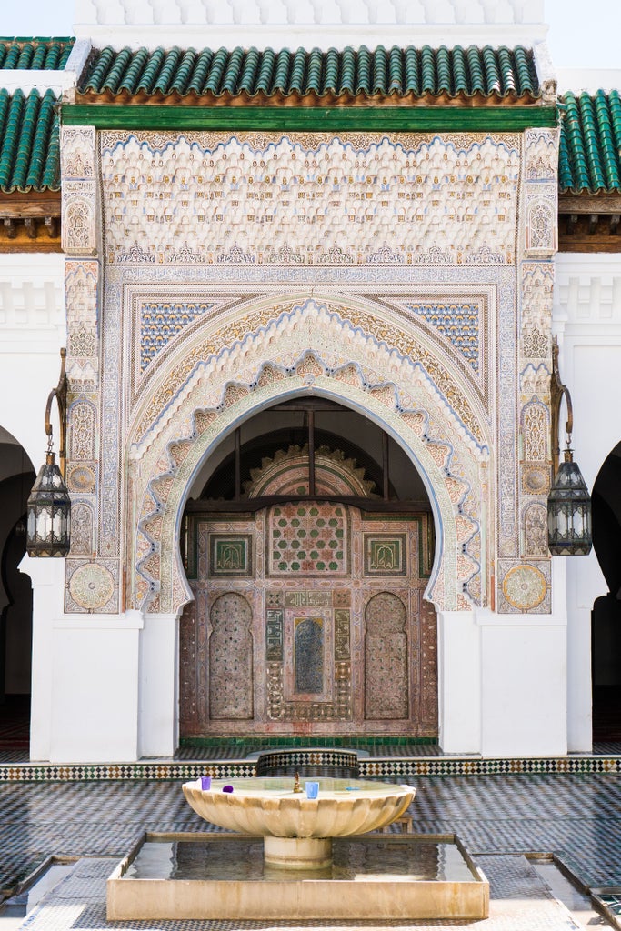 Traditional arched entrance with intricate Moroccan tilework leads to a narrow cobblestone street lined with local shops in Fez medina