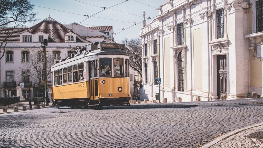 Historic Lisbon cityscape with terracotta roofs, gleaming white buildings and iconic Rua Augusta Arch framed by sunny blue skies