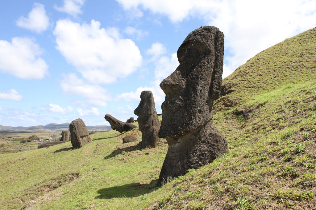 Towering Moai statues stand against dramatic ocean cliffs on Easter Island, sunlight casting long shadows across rugged terrain