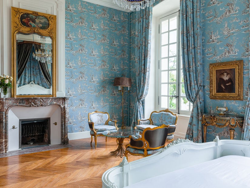 Opulent French château hotel room with elegant period furniture, crystal chandelier, ornate crown molding and sweeping countryside views