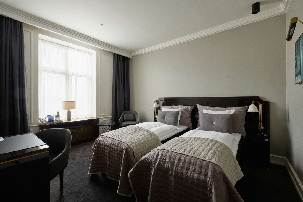 Elegant twin deluxe hotel room with modern Danish design, featuring plush white bedding, sleek furniture, and soft neutral color palette in Copenhagen