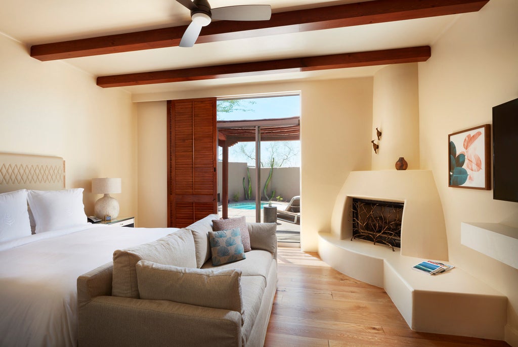 Desert-style luxury resort with adobe buildings nestled among saguaro cacti, featuring a turquoise pool and dramatic mountain backdrop