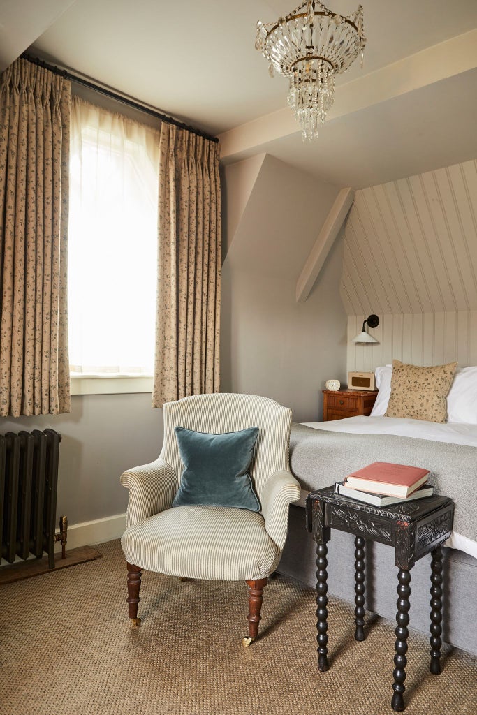 Cozy coastal hotel room with nautical-inspired decor, white linens, natural wood accents, and panoramic ocean view from large window at seaside retreat