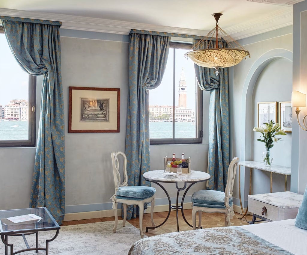 Elegant hotel room with ornate gold-framed mirrors, silk drapes, and stunning views of Venice's St. Mark's Square through floor-to-ceiling windows