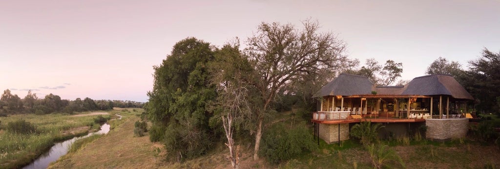 Elegant safari lodge overlooking African bushveld, featuring infinity pool and expansive wooden deck with panoramic river views