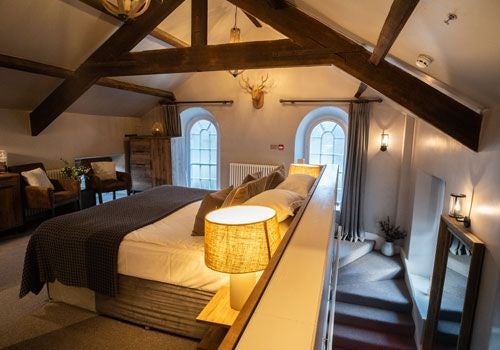 Luxurious bedroom at Yorebridge House with plush white bedding, elegant decor, and soft natural light illuminating wooden floors and countryside views.