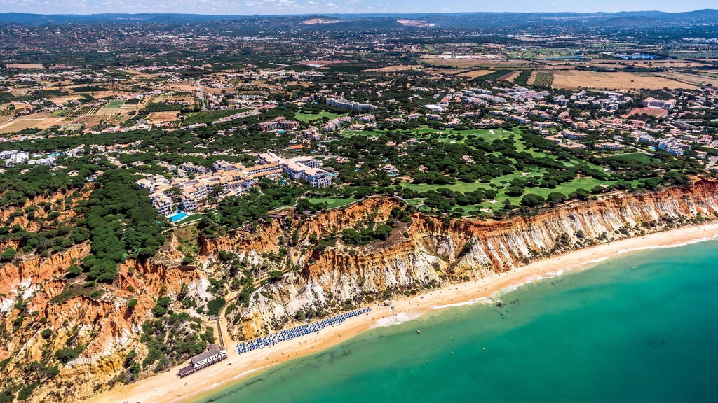 Elegant five-star beachfront hotel with terracotta roofs nestled atop red sandstone cliffs, overlooking turquoise Atlantic Ocean