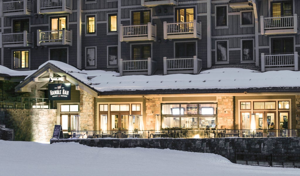 Snow-covered luxury mountain resort with stone and wood facade, featuring grand entrance, expansive windows and rustic alpine architecture