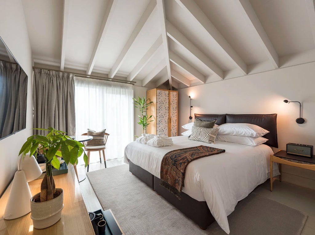 Modern loft-style hotel room with exposed brick walls, hardwood floors, elegant furnishings, and natural light streaming through arched windows