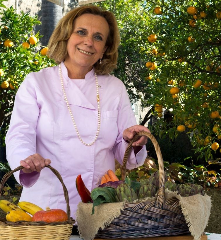 Professional chef demonstrates pasta-making technique in rustic Tuscan kitchen, surrounded by fresh ingredients and copper cookware.