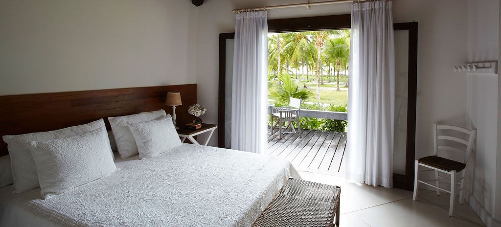 Luxurious Brazilian bungalow suite with elegant wooden decor, soft lighting, plush bed, and panoramic view of tropical landscape at Fazenda resort