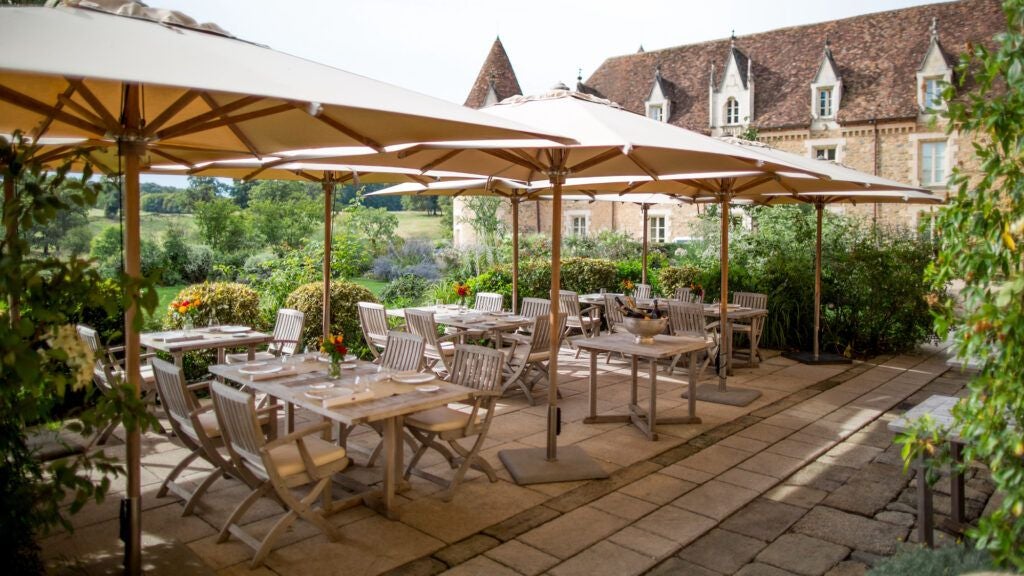 Elegant French countryside château with stone exterior, surrounded by lush green gardens and tranquil reflecting ponds at golden hour