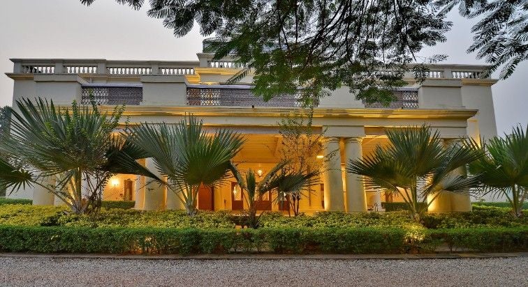 Elegant colonial-style luxury palace hotel with white facade, grand pillars, and manicured gardens set against a clear blue Indian sky