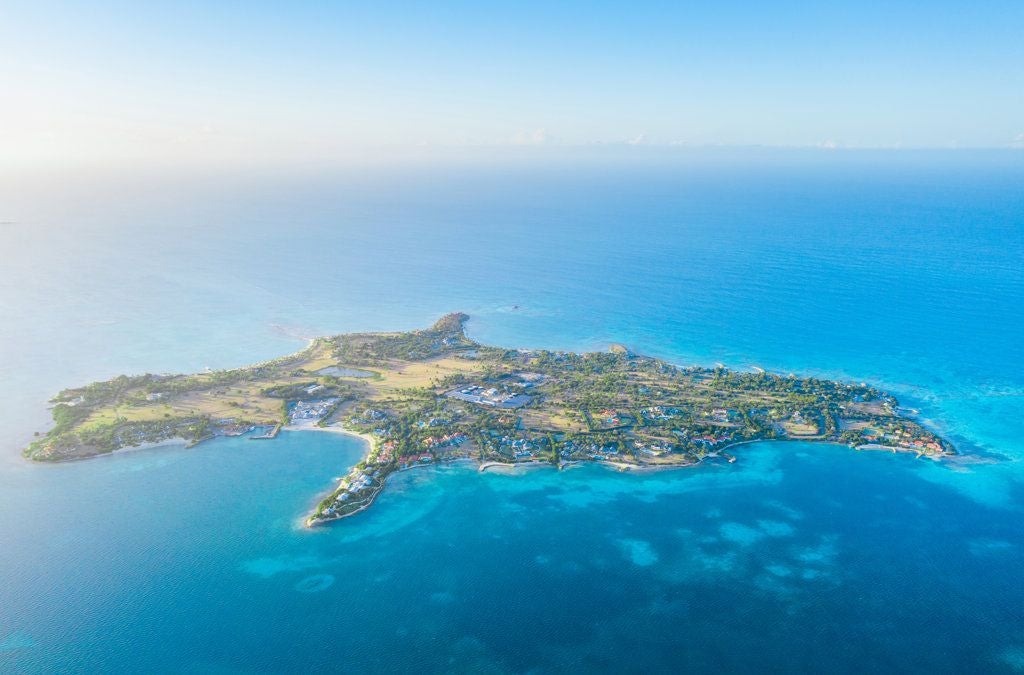 Luxurious beachfront resort with white sandy shore, turquoise Caribbean waters, and elegant palm-lined tropical landscape at scenic island retreat