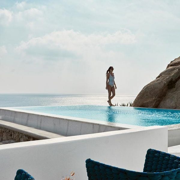 Luxurious white-walled suite with minimal design, panoramic Aegean Sea view, infinity pool, minimalist furniture, and golden sunset lighting in Greece