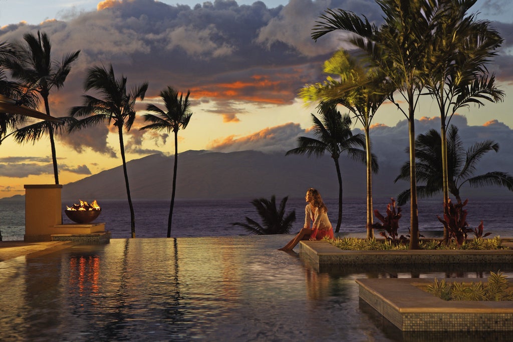 Beachfront luxury resort in Maui with infinity pools overlooking the Pacific Ocean, surrounded by swaying palm trees at sunset