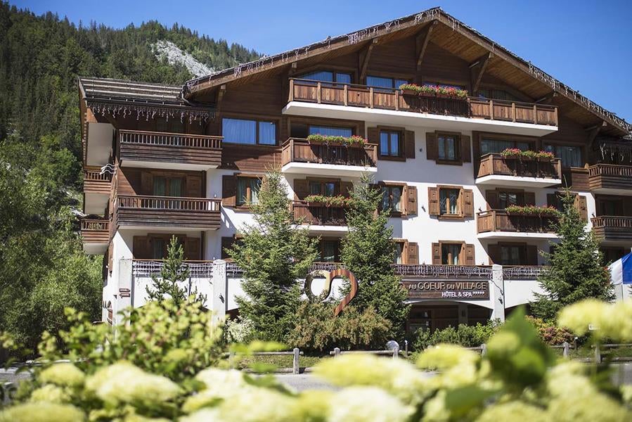 Luxurious mountain spa hotel featuring traditional Alpine architecture with wooden balconies, stone facade, and snow-capped peaks backdrop