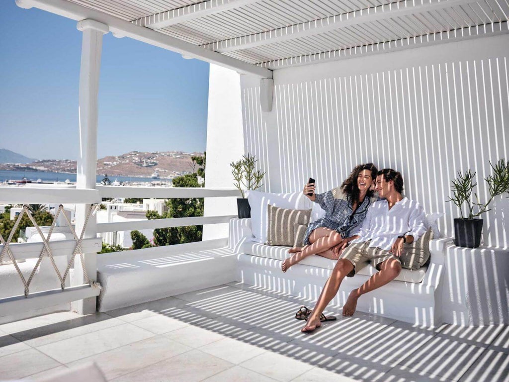 White luxury hotel with traditional Cycladic architecture, infinity pool overlooking Mykonos sea, curved balconies at sunset