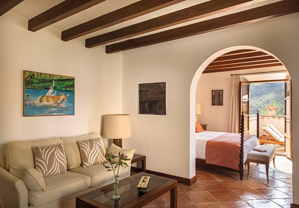 Elegant junior suite with rustic stone walls, wrought iron bed, sitting area, and arched doorway leading to a private terrace in Mallorca