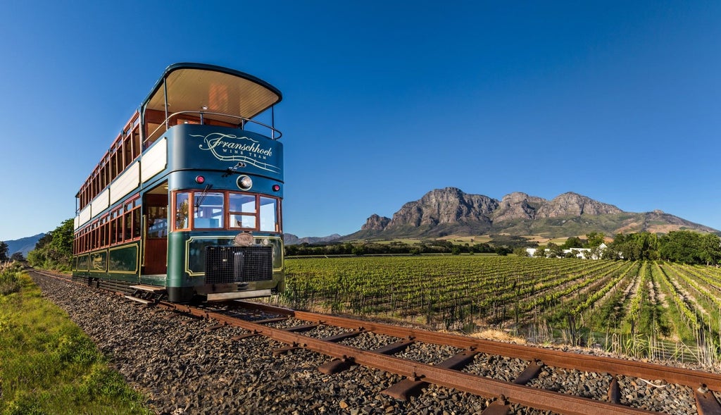 Historic Cape Dutch wine estate nestled in Franschhoek Valley, featuring elegant whitewashed buildings and manicured gardens framed by mountains