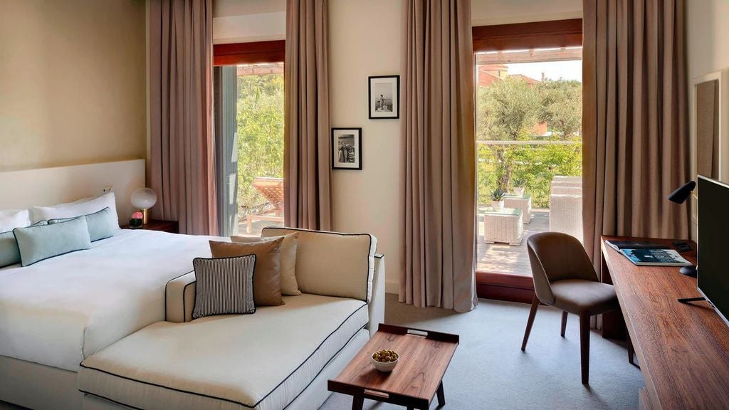 Elegant hotel room with king bed, white linens, floor-to-ceiling windows overlooking Venice lagoon, modern furnishings and marble bathroom