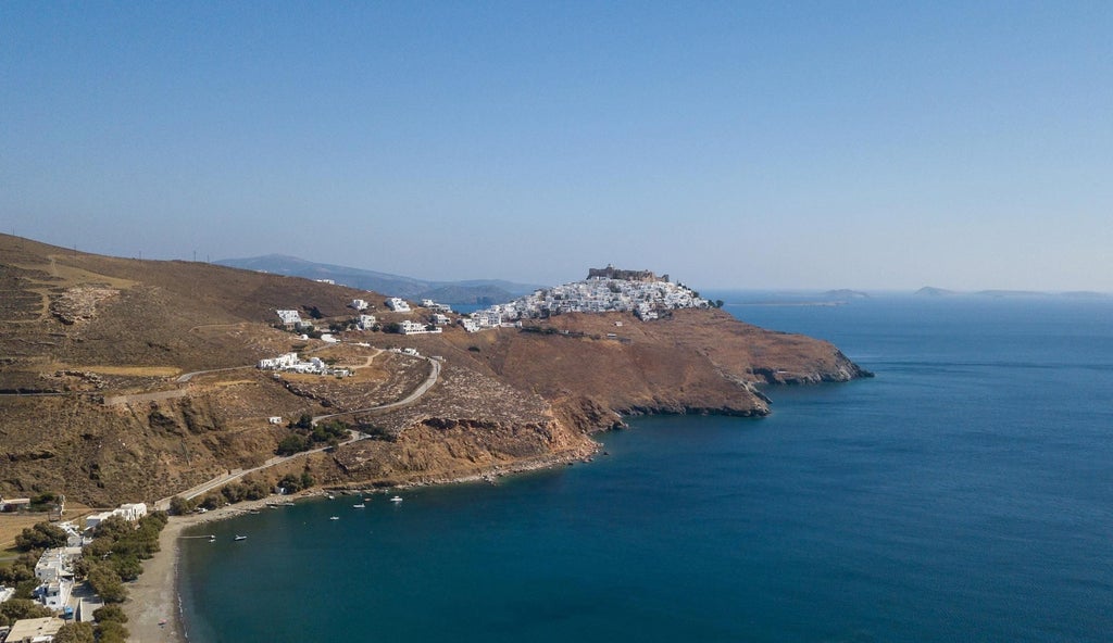 Luxurious Greek boutique hotel suite with white stone walls, elegant minimalist decor, and panoramic Aegean Sea view from private balcony at sunset