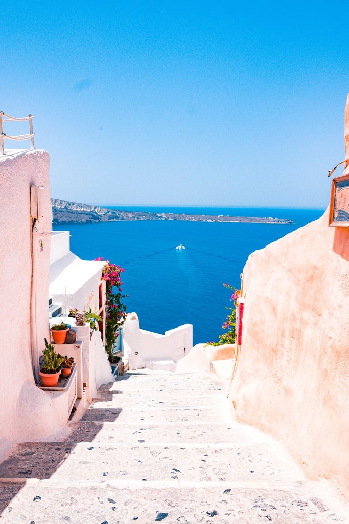 Greek sunset over the Aegean Sea with white-washed Cycladic buildings cascading down cliffs, domed blue church in foreground