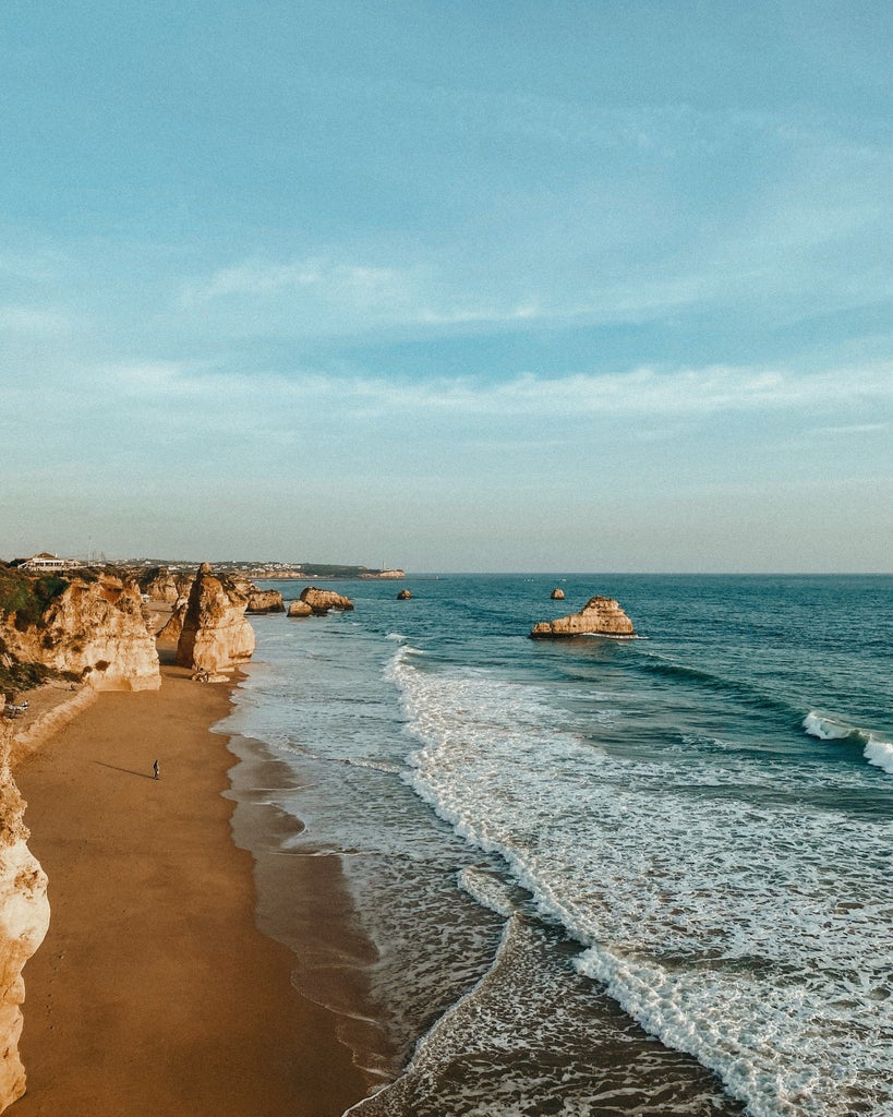 Rugged limestone cliffs tower above pristine turquoise waters, with luxury villas perched along the golden coastline of Portugal's Algarve