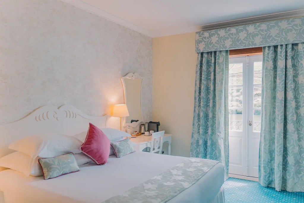 Elegant junior suite with vintage-inspired decor, plush king bed, rich wooden furnishings, and large windows overlooking scenic Portuguese landscape