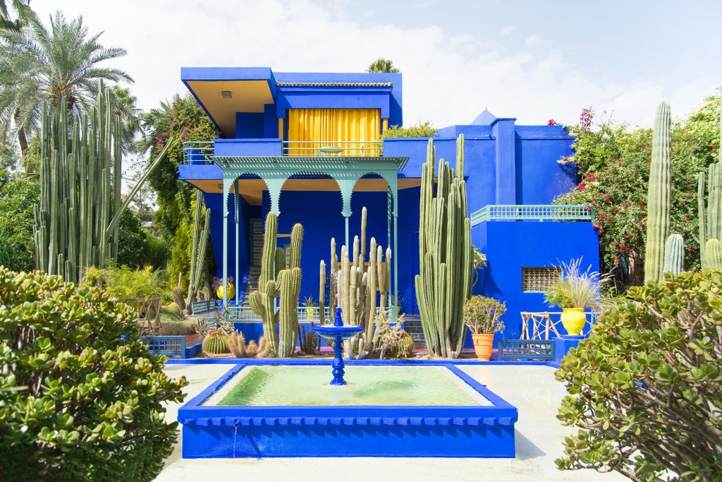 Ornate Moroccan riad courtyard in Marrakech with traditional tilework, flowing fountain and luxurious cushioned seating under arched walkways