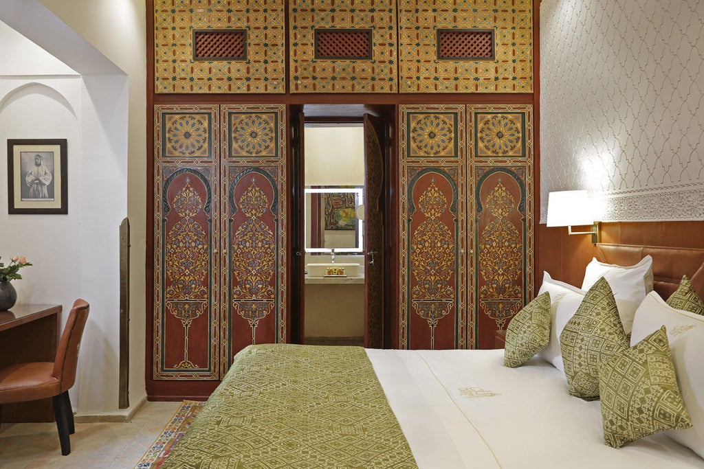 Elegant Moroccan hotel facade with ornate archways, traditional lanterns, and lush greenery framing a stone courtyard entrance