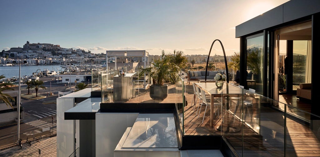 Luxurious penthouse suite at Sir Joan Hotel with modern minimalist design, white decor, panoramic windows overlooking Spanish cityscape at sunset