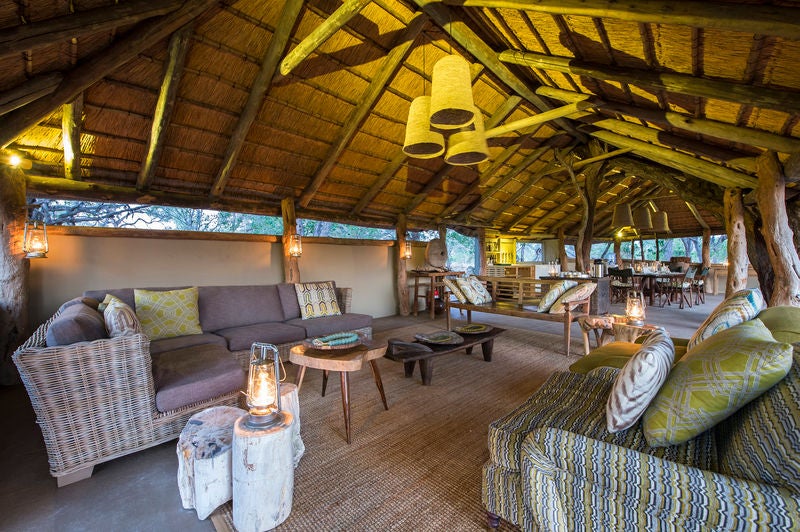 Elevated luxury safari tent overlooking pristine African wetland with wooden deck, canvas walls and thatched roof at sunset