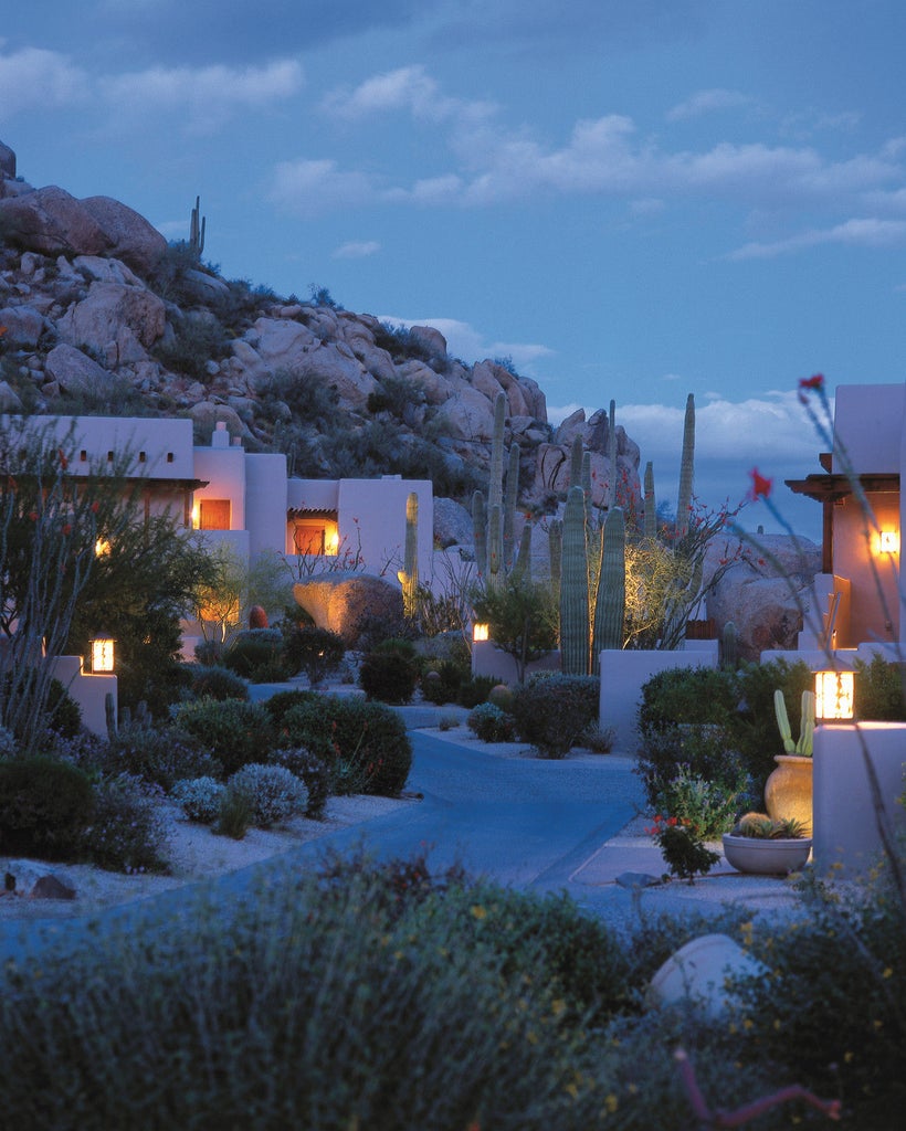 Luxury desert resort with adobe-style architecture, towering cacti and dramatic mountain backdrop at golden hour in Scottsdale, Arizona