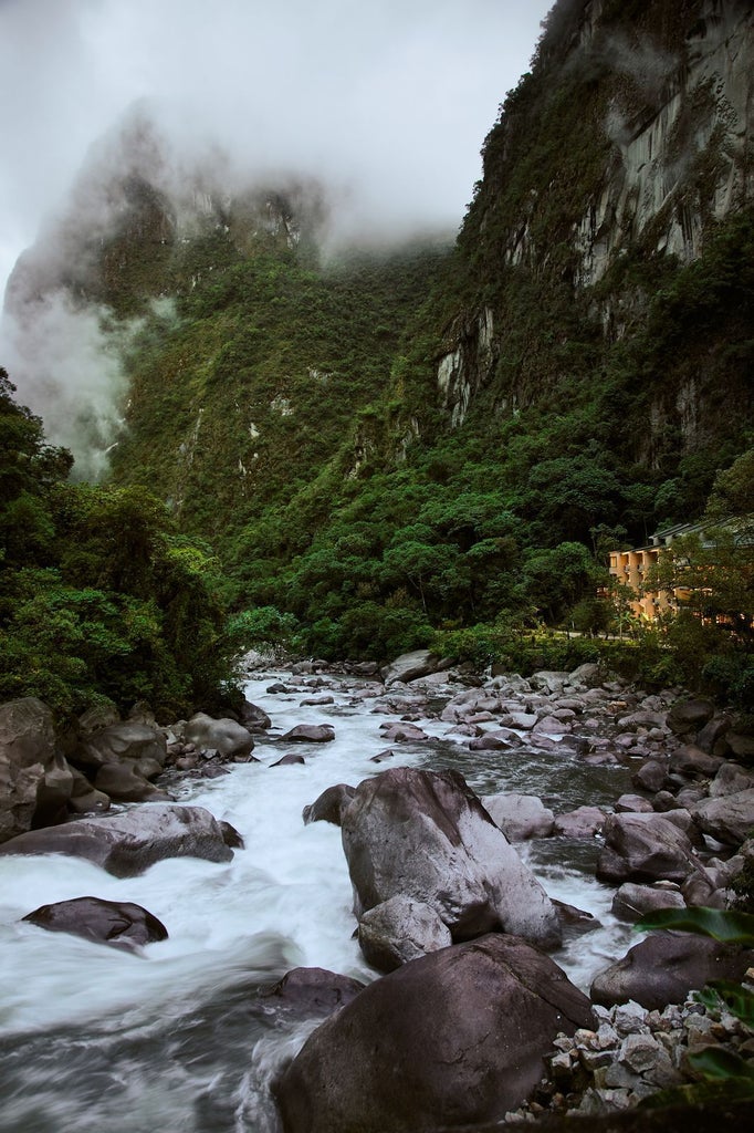 Elegant mountain lodge hotel with stone and wood facade nestled beneath Machu Picchu's peaks, surrounded by lush Andean vegetation