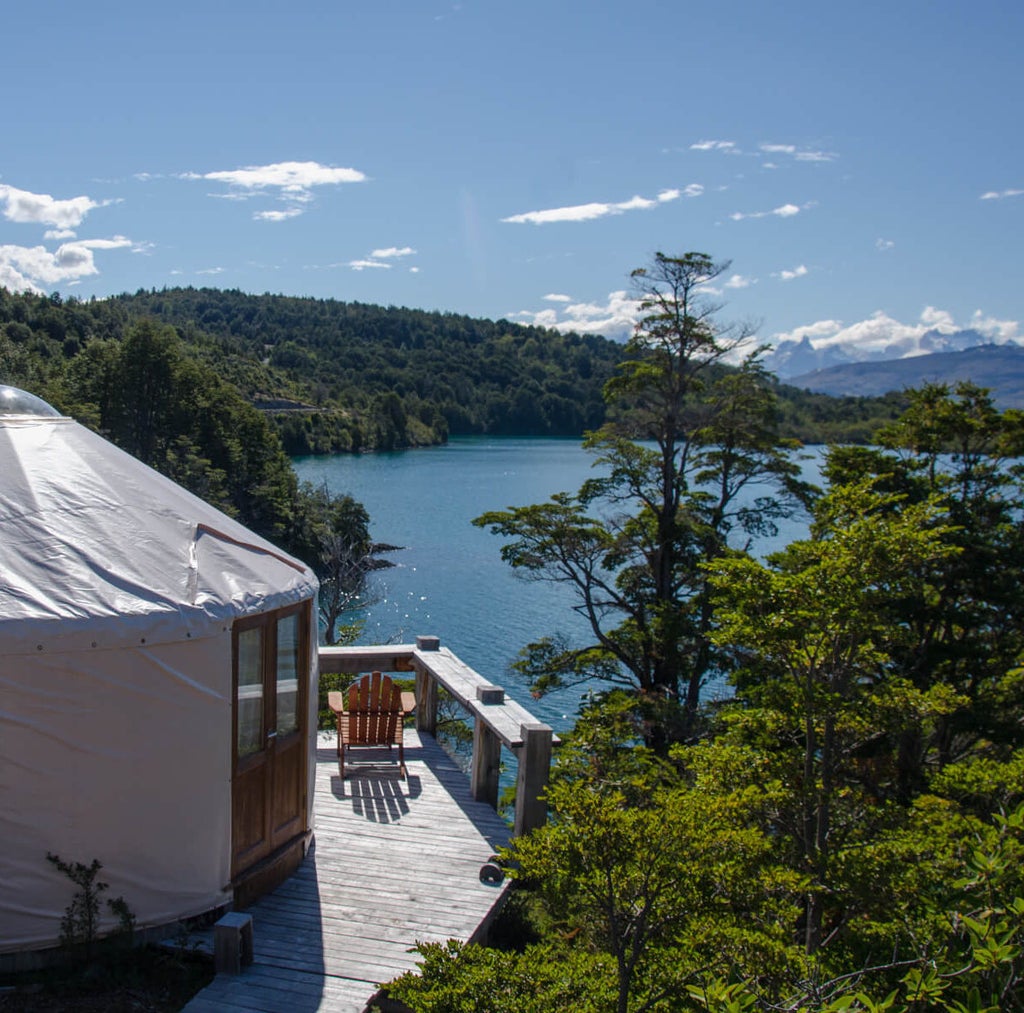 Modern luxury yurt nestled in Patagonian wilderness, circular tent with wood deck overlooking snow-capped mountains and pristine lake