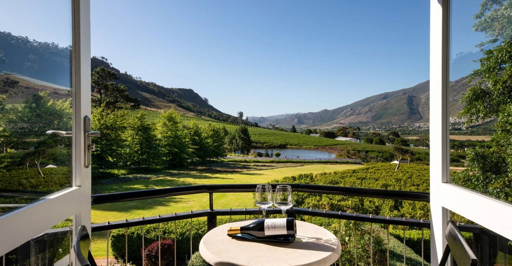 Elegant Shiraz Room at Mont Rochelle wine estate, featuring plush white bedding, wood-accented furnishings, and a serene South African mountain landscape view