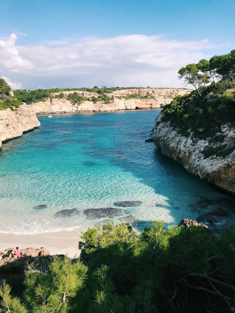 Mediterranean coastal villa in Mallorca with infinity pool overlooking turquoise sea, framed by lush gardens and limestone cliffs