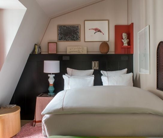 Elegant Parisian hotel room with plush dark blue walls, luxurious king bed, vintage gold-framed mirror, and sophisticated minimalist decor