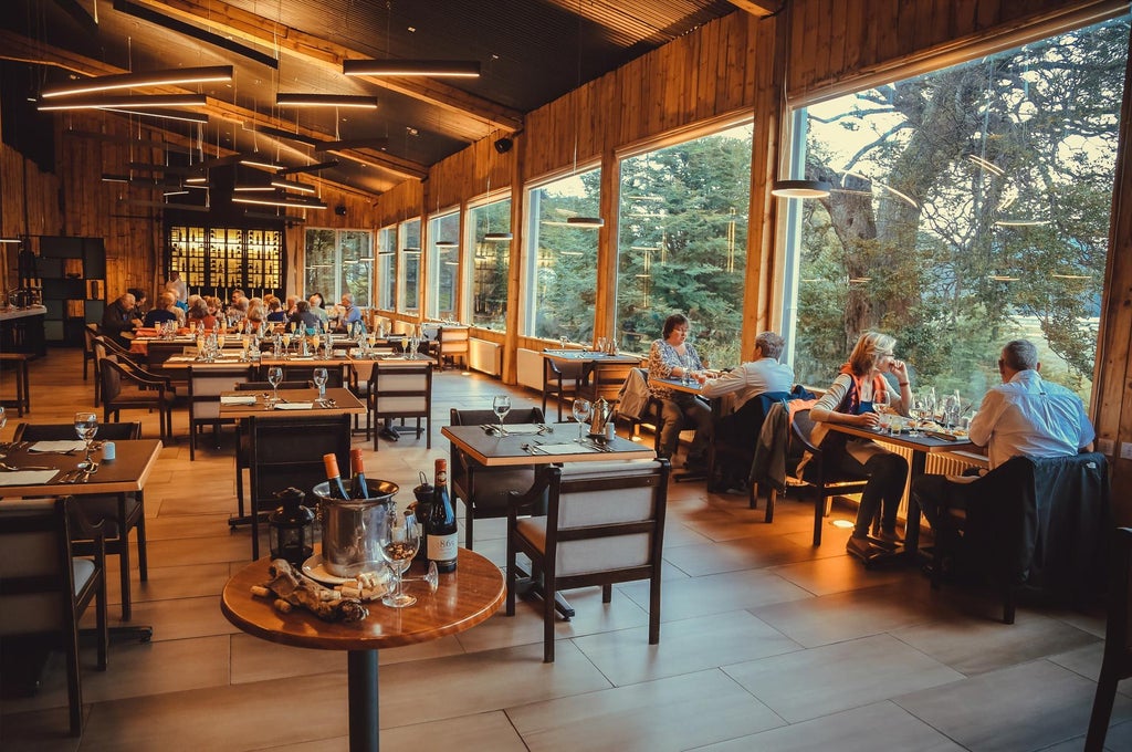 Luxury mountain lodge with wooden facade nestled against snow-capped Patagonian peaks, reflecting on the calm waters of Grey Lake, Chile